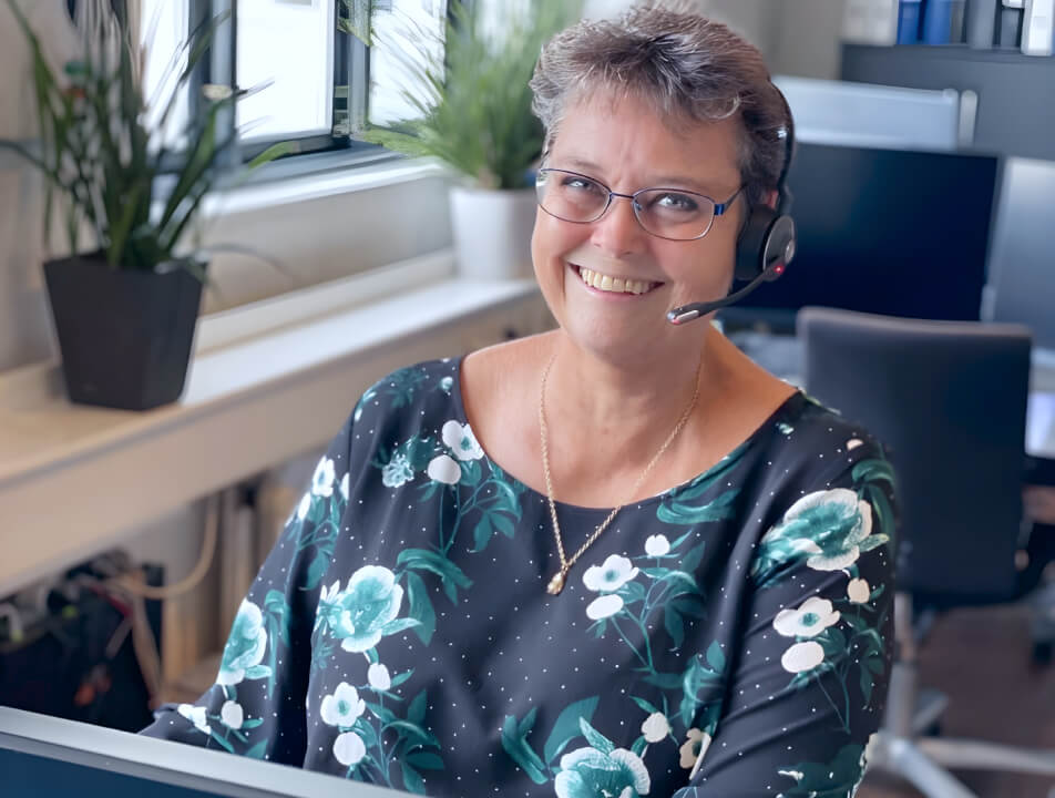 Eine Frau mit Headset lächelt, während sie an einem Computer arbeitet.