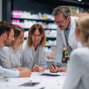 Kommunikation in der Apotheke Fünf Personen in weißen Kitteln diskutieren in einem Raum.